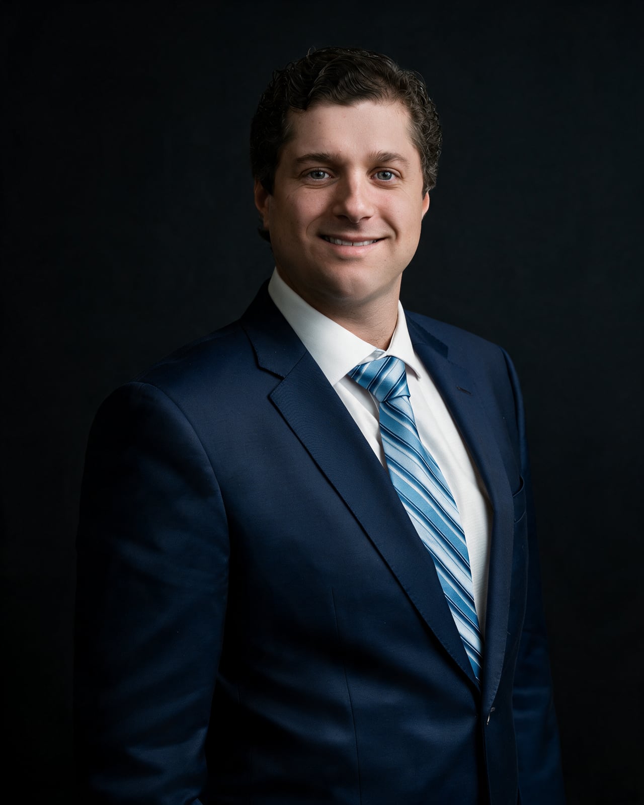 Spencer Nyman in a navy suit against a dark background.
